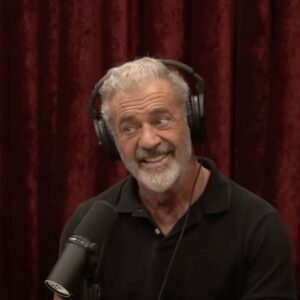 Mel Gibson in front of a red curtain being interviewed by Joe Rogan