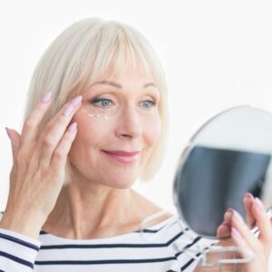 woman applying anti-wrinkle cream under her eye while looking in a hand mirror
